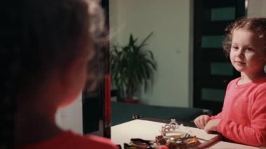 little cute girl in pink dress looks at her reflection in the mirror