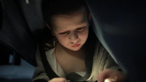 Piccolo ragazzo sotto la coperta sta giocando un gioco sul suo smartphone cellulare di notte — Video Stock