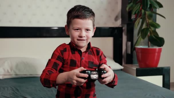 Милый мальчик играет в видеоигру, держит джойстик, эмоционально проводит время — стоковое видео
