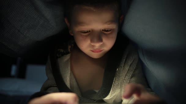 Little guy under the blanket is playing a game on his phone smartphone at night — Wideo stockowe