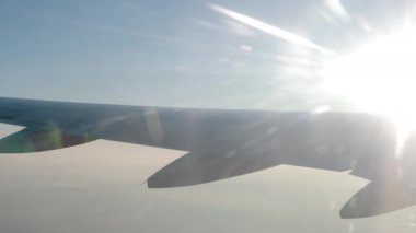 Havada uçan bir uçağın kanadı, yavaş çekim, biraz sis ve güneş ışığı..