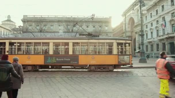 Orange tram goes through city. People are standing at bus stop, near white taxi — Stock Video