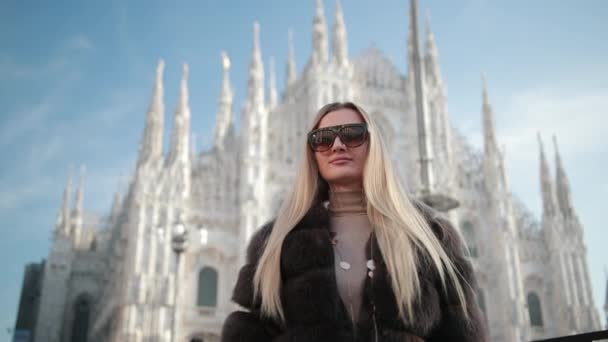 Жінка-блондинка Сонячні окуляри У хутряних мундирах Пози проти тла Дуомо в Мілані. — стокове відео