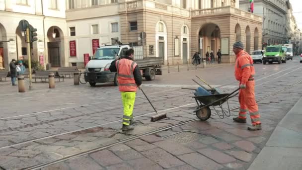 Trabajadores de la carretera reparan la carretera en uniformes naranjas con una pala y una carretilla . — Vídeos de Stock