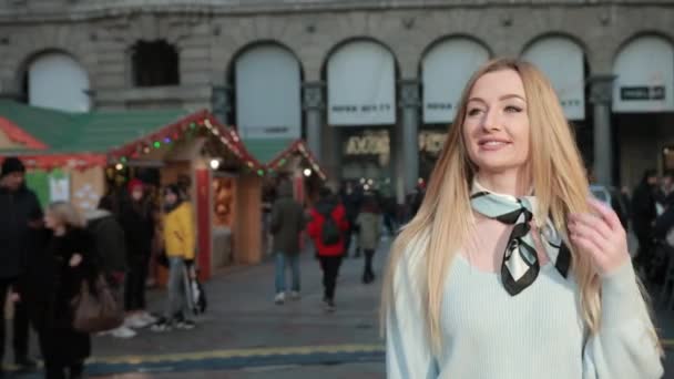A fiatal szőke nő végigsétál a karácsonyi piacon, vásár, mosoly. Napsütés. — Stock videók