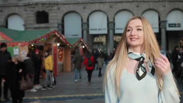 Mujer rubia joven camina por el mercado de Navidad, justo, sonríe. Día soleado . — Vídeo de stock