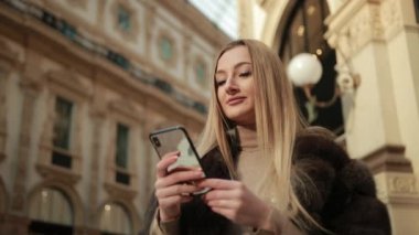 Genç Sarışın Kadın, alışveriş merkezinde telefonla konuşuyor. Kürk manto giymiş.