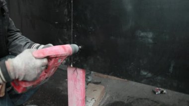 İnşaat işçisi ahşap çitte delik açıyor, metal telle bağlanıyor. Kapat.