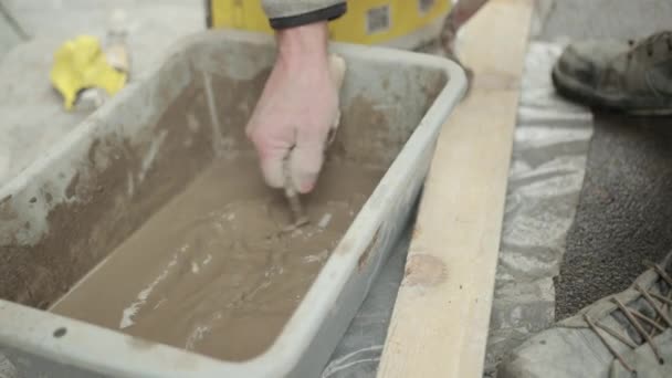 Une main de Mans avec la spatule mélange la solution liquide dans la brouette pour la construction — Video