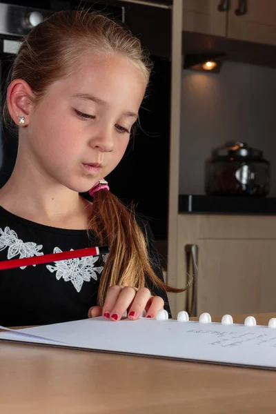 Mladá dívka, myslet a dělat domácí úkoly v kuchyni u stolu drží tužku — Stock fotografie