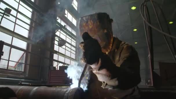 Сварщик в маске сваривает трубу сваркой в цехе завода — стоковое видео