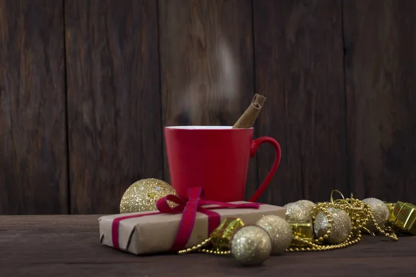 Red cup, cinnamon, gift wrapping, decorative toys on a wooden ba — Stock Photo, Image