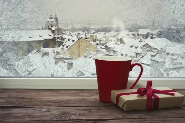 Egy befagyott ablak és egy piros pohár és az ablakpárkányon, ajándék — Stock Fotó