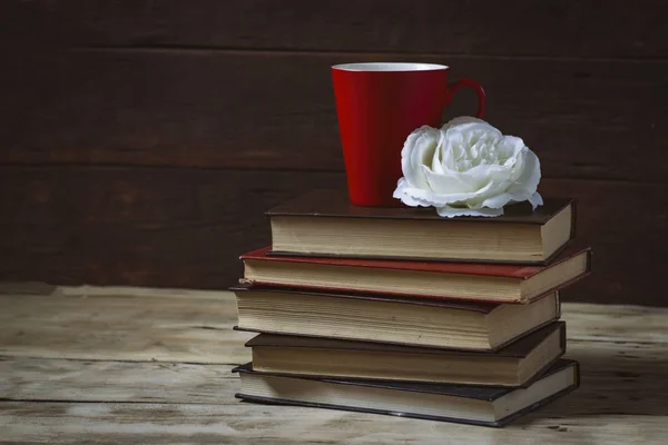 White rose, books and a red cup. Composition on a wooden backgro
