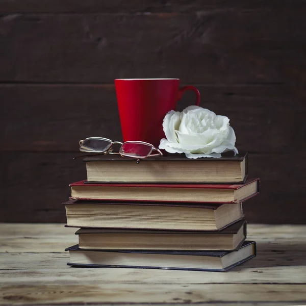 Rosa, livros, óculos e um copo vermelho. Composição em umas costas de madeira — Fotografia de Stock