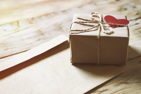 On a wooden table an envelope and a gift box with a heart — Stock Photo, Image
