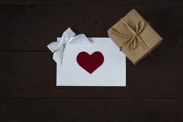 Enveloppe avec un cœur, un arc somptueux et une boîte cadeau sur un bac de rosée — Photo
