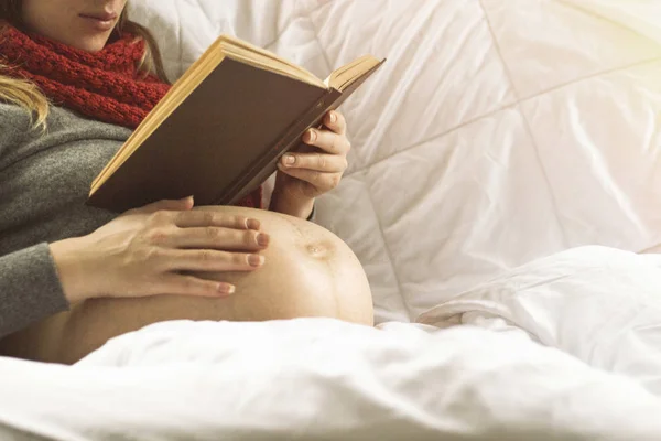 Mujer embarazada en la cama leyendo un libro — Foto de Stock