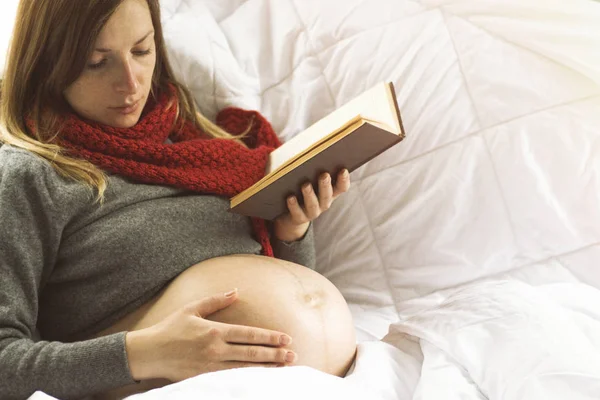 Schwangere liegt im Bett und liest ein Buch — Stockfoto