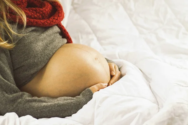 Pregnant woman in a gray sweater holding her belly with her hand — Stock Photo, Image