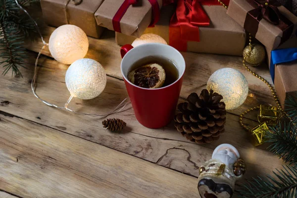 Santa Claus, cup with tea, gifts, fir cones and garlands on a wo