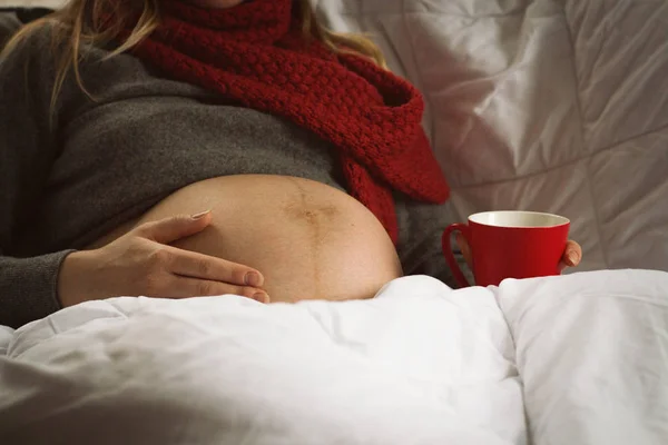 Schwangere junge Frau hält Händchenbauch und trinkt Tee im Bett — Stockfoto