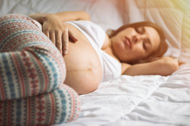 Hamile genç kız uyuyor ve onun stom elini tutarak