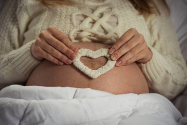 Hamile karnı üzerinde beyaz bir kalp el yapımı tutar