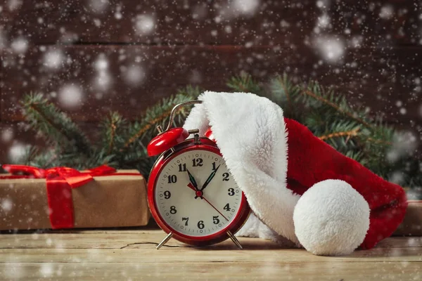 Санта Клауса капелюх на годиннику. Подарунок і ялин гілки. Снігопад — стокове фото
