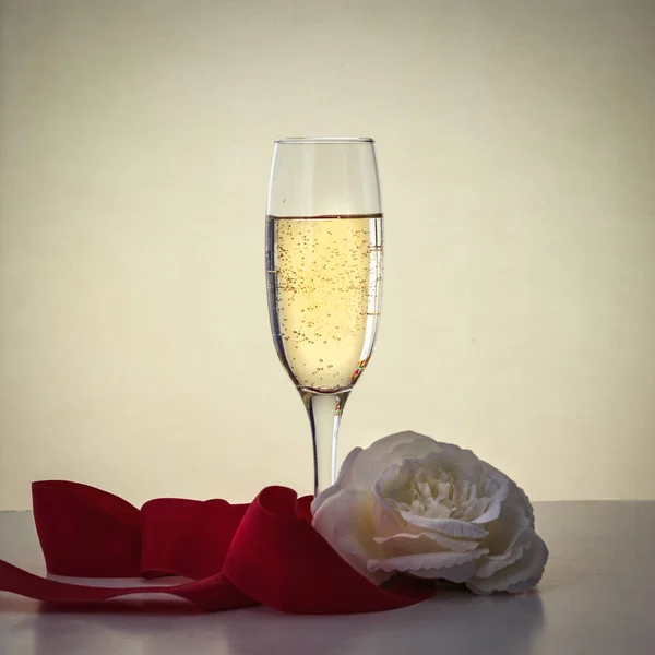 Bir bardak şampanya, beyaz bir gül ve bir kırmızı kurdele — Stok fotoğraf