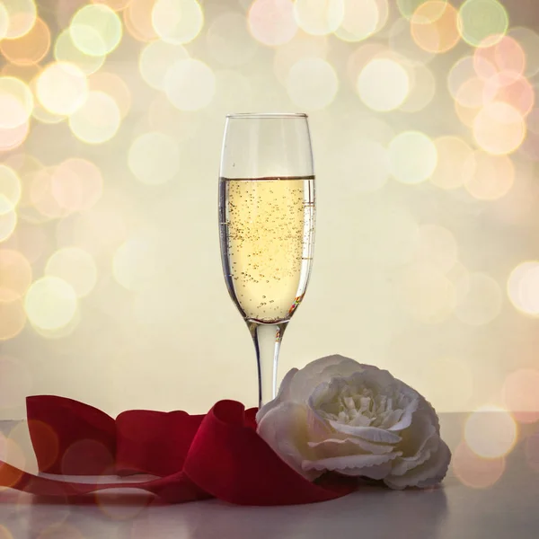 Bir kadeh şampanya, beyaz gül ve kırmızı kurdele. Bokeh — Stok fotoğraf