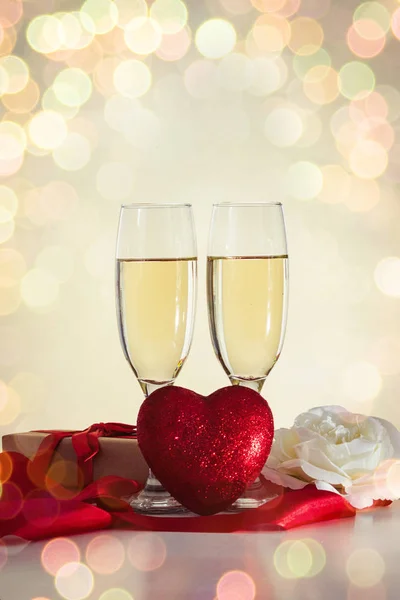 Two glasses with champagne, a gift wrapped, a heart, a red ribbo — Stock Photo, Image