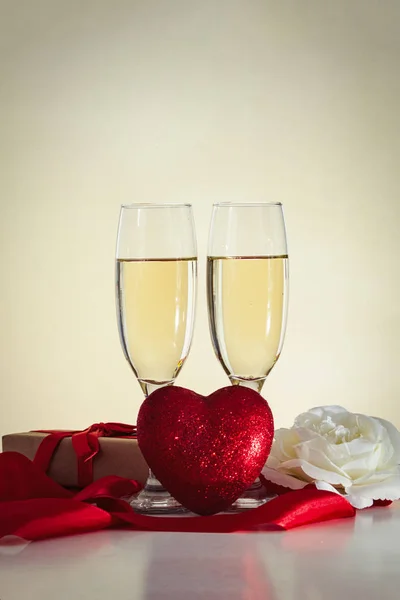 Two glasses with champagne, a gift wrapped, a heart, a white ros — Stock Photo, Image