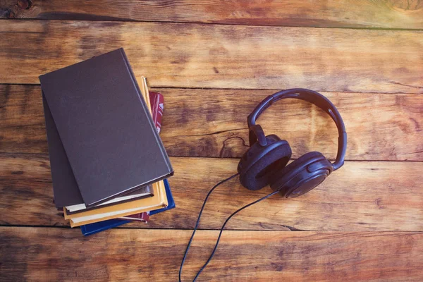 Hoofdtelefoons en een stapel boeken op de houten achtergrond. Audiobo — Stockfoto