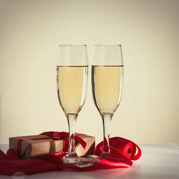 Paketlenmiş hediye, iki bardak şampanya ve kırmızı kurdele. — Stok fotoğraf