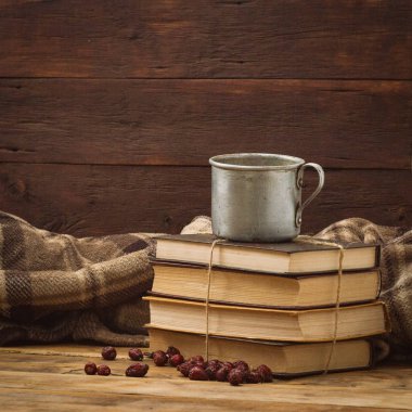 Metal bir fincan sıcak çay, kahve, sıcak bir battaniye, kitap yığını ile