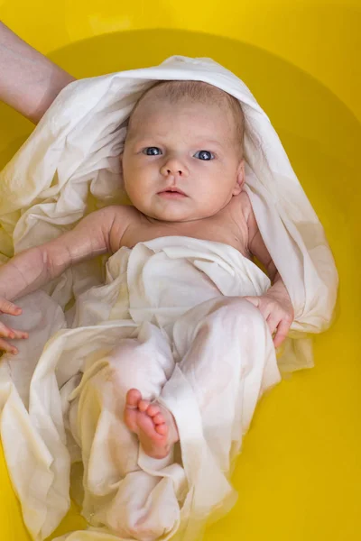 Новорожденный в белом фильме купается в жёлтой ванне, держит маму — стоковое фото