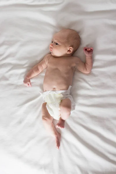 Малыш в подгузнике лежит на белой кровати. Белый — стоковое фото