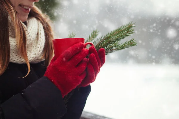 Young Girl in Red Gloves holds a Red Cup with Hot Tea and Spruce