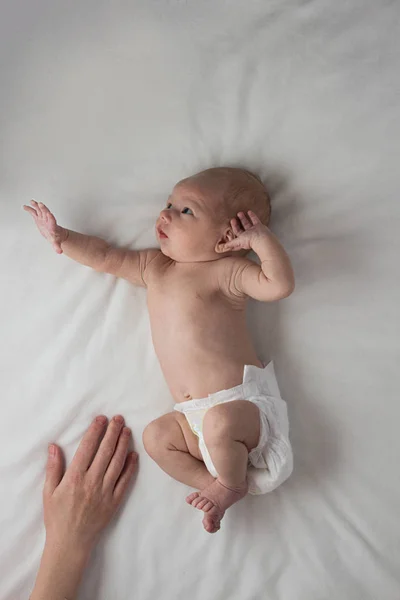 Un pequeño bebé en un pañal, bebé, se encuentra en una cama blanca y una mujer —  Fotos de Stock