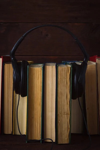 Auriculares colocados en libros plegados sobre el fondo de madera oscura — Foto de Stock