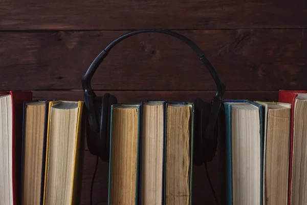 Auriculares colocados en libros plegados sobre el fondo de madera oscura — Foto de Stock