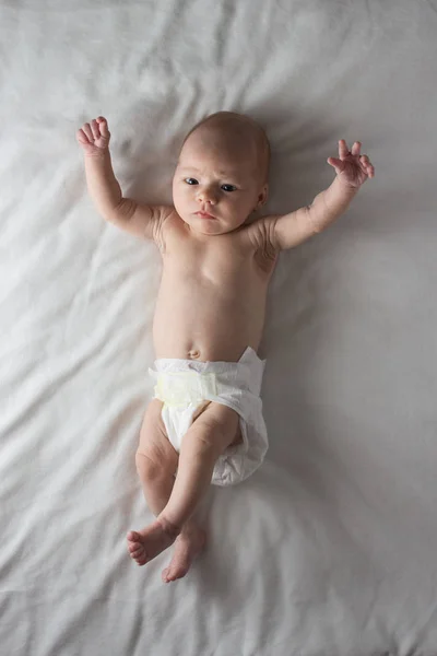 Bebé en un pañal blanco acostado sobre una manta blanca. Fondo blanco — Foto de Stock
