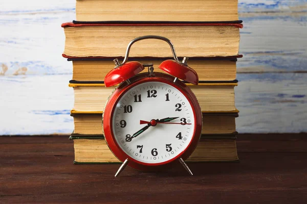 Reloj despertador rojo y una pila de libros sobre fondo de madera — Foto de Stock