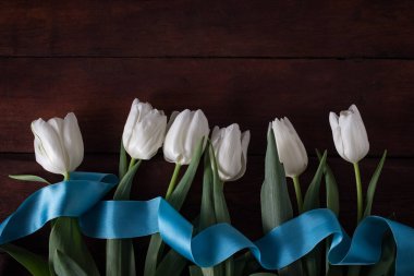 Beyaz Laleler ve koyu ahşap zemin üzerine mavi kurdele. Concep