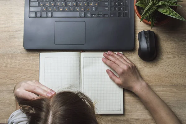 Young girl bent over a diary and a laptop in a working environment. The concept of a long and hard day, fatigue, lack of sleep.Top View