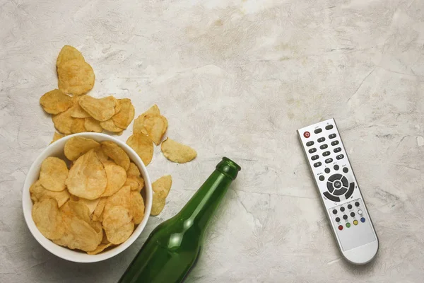 TV-fjärrkontroll, en skål med chips och en flaska öl på en ljus backg — Stockfoto