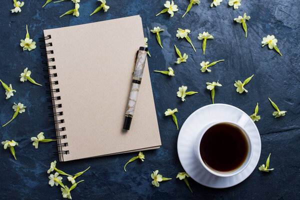 Cup of coffee, notebook and flowers on a dark blue background. F