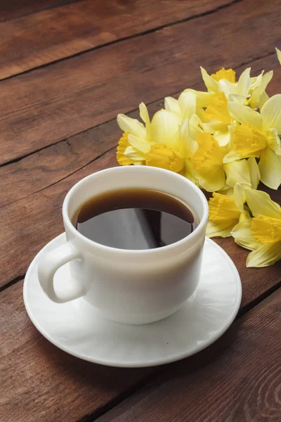 Cup of coffee, Spring flower Narcissus on a dark wooden backgrou