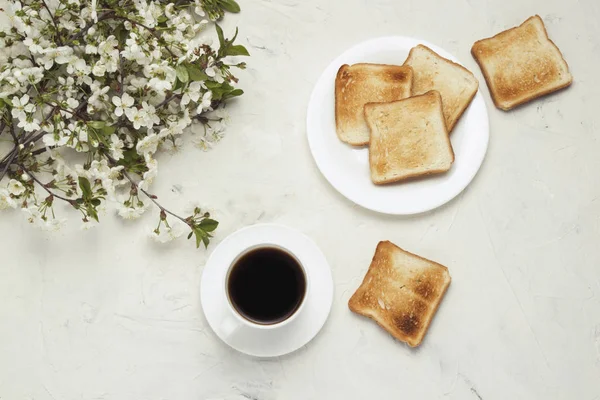 White Cup with Black Coffee, Toast, Jem and Spring Flowers on the Light Stone Background. The concept of a Healthy Breakfast. Flat lay, top view.